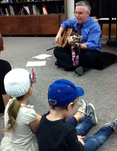 Andrew Walker playing a guitar for a group of children
